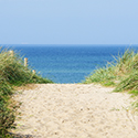 Blick vom Deich auf das Meer, links und rechts liegen leicht bewachsene Sanddünen